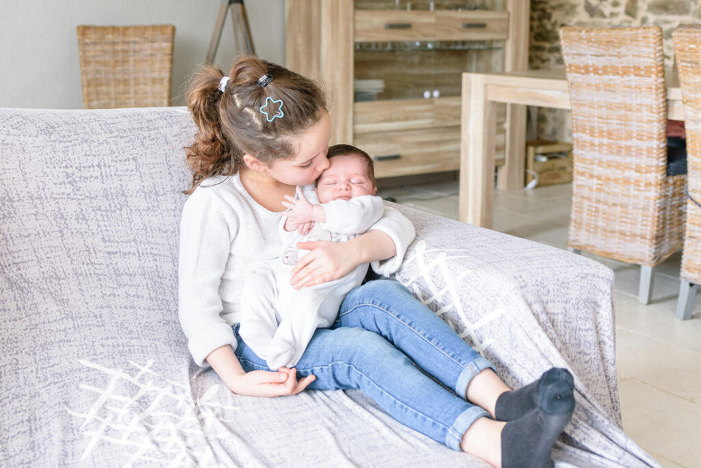 La grande sœur prend son petit frère dans ses bras.