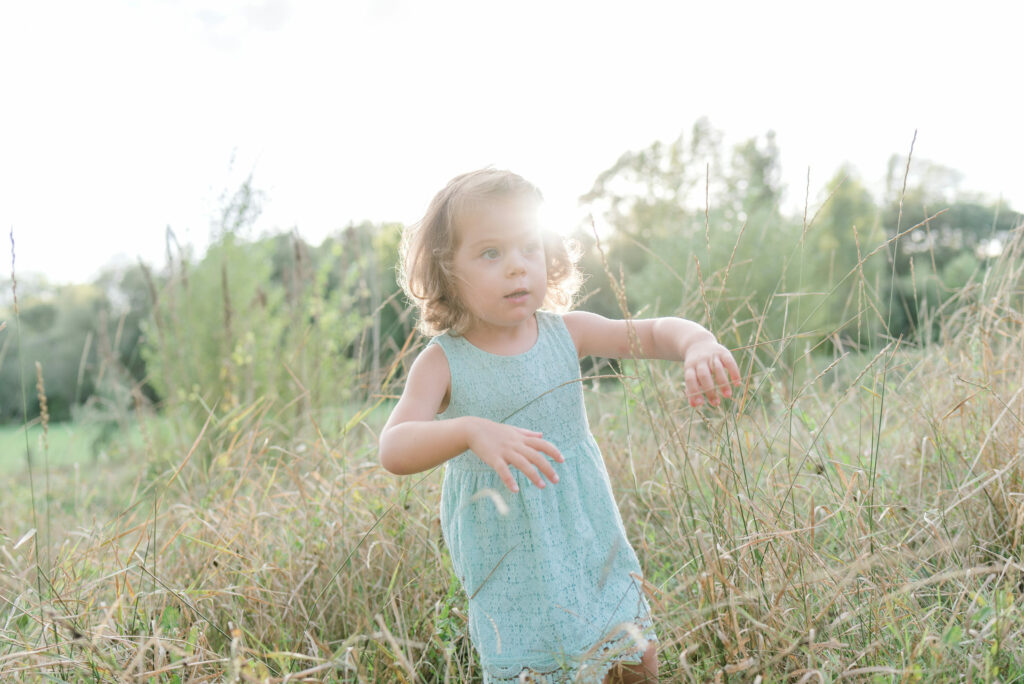 Une petite fille pose pour une photo avec le soleil en arrière-plan. Photographe de famille à Angers.