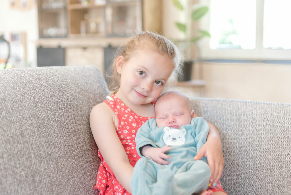 Une petite soeur tient dans ses bras Son petit frère qui vient de sortir de la maternité